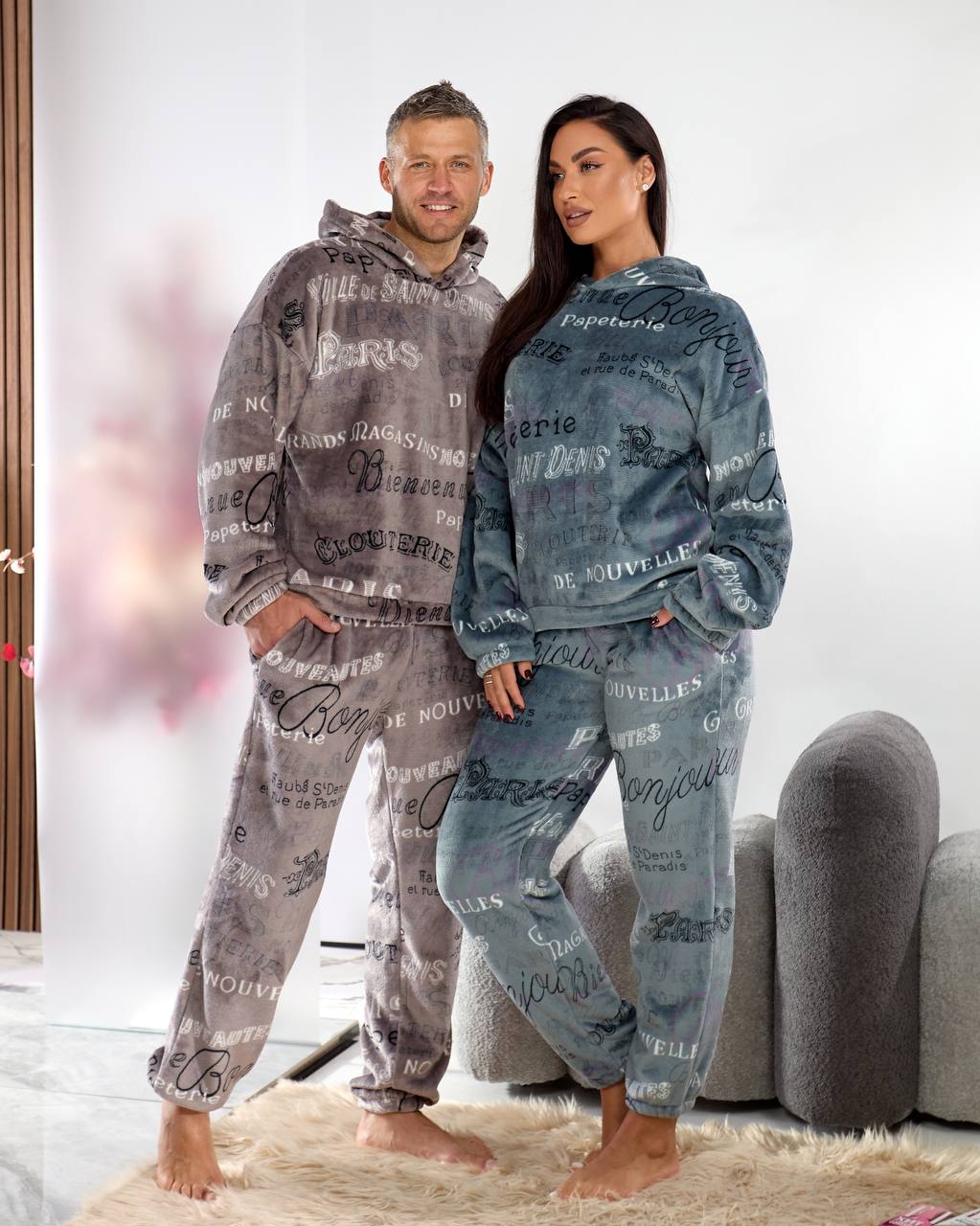 Two people wearing matching pajama sets with text patterns in a living room.