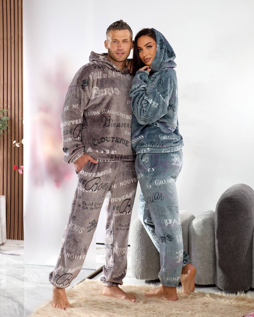 Two people wearing matching pajama sets with text design in a room.