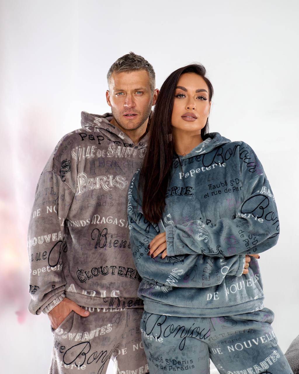 Two people wearing matching gray and blue hoodies with text design on a white background
