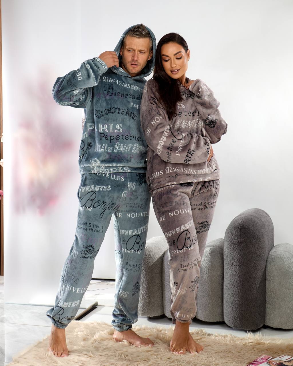 Two people wearing matching pajama sets with text design in a living room.