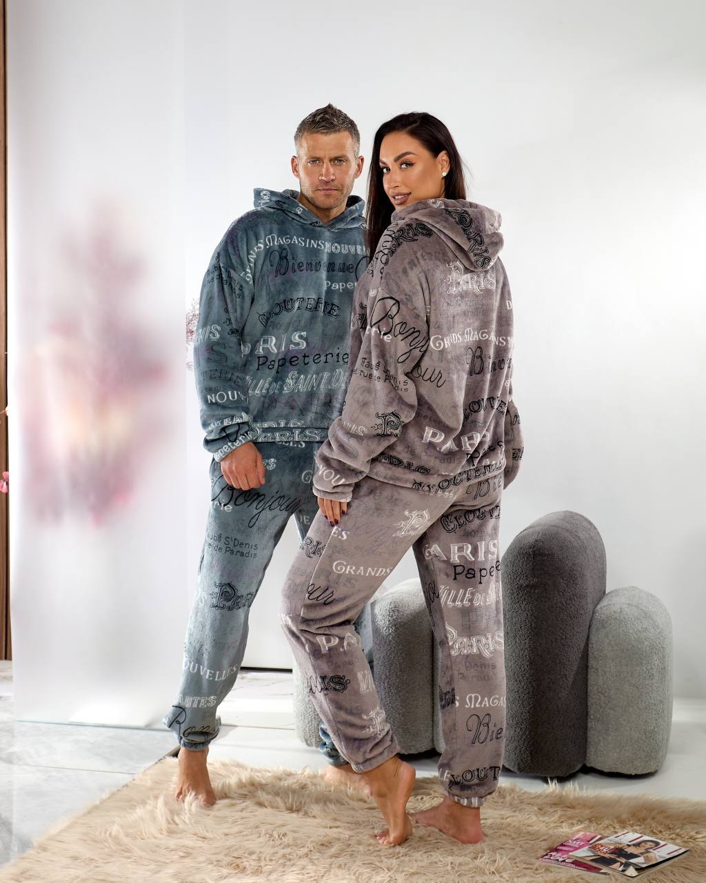 Two people wearing matching gray and blue pajama sets with text patterns in a room.