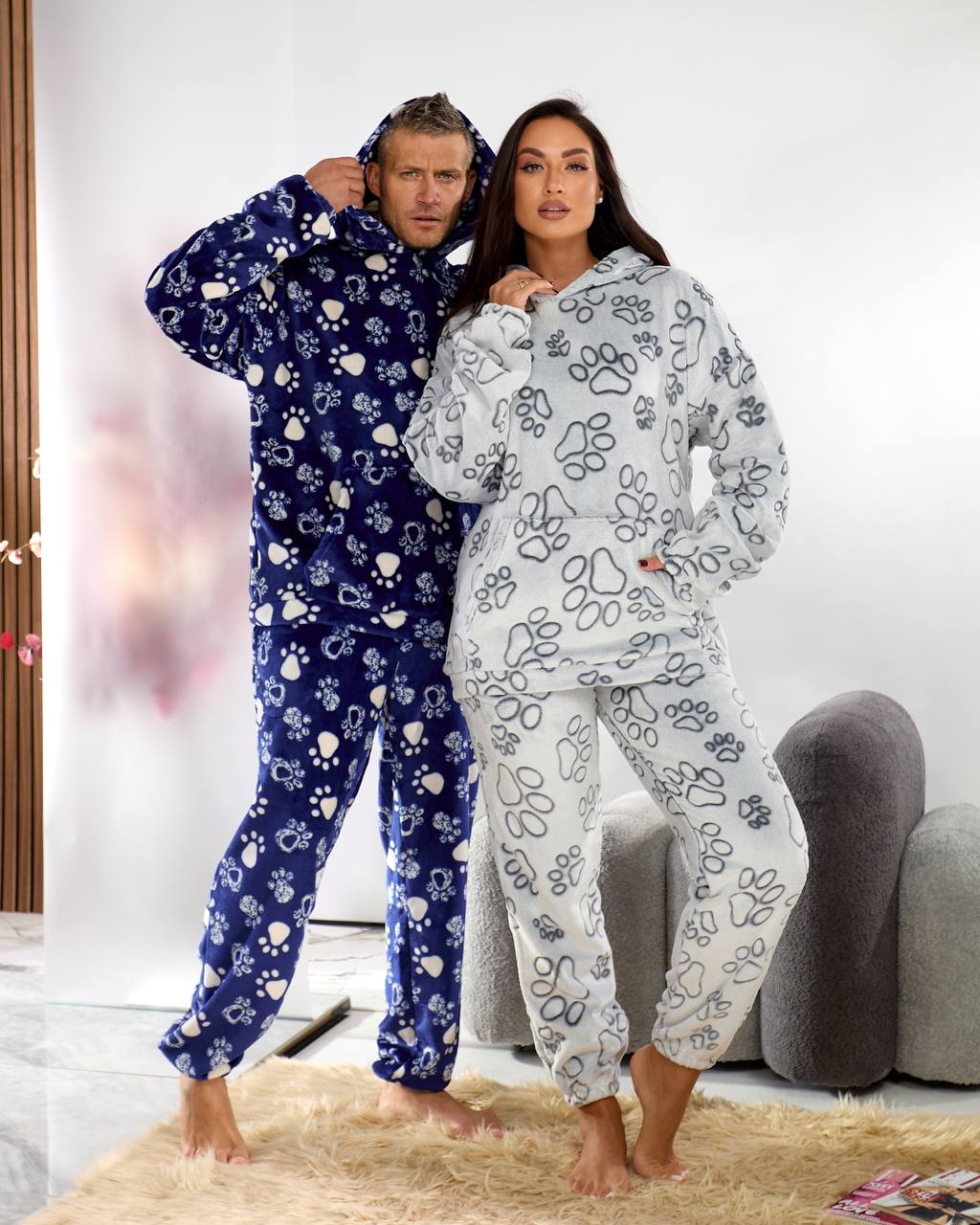 Two people wearing matching onesies with paw prints in a cozy room.