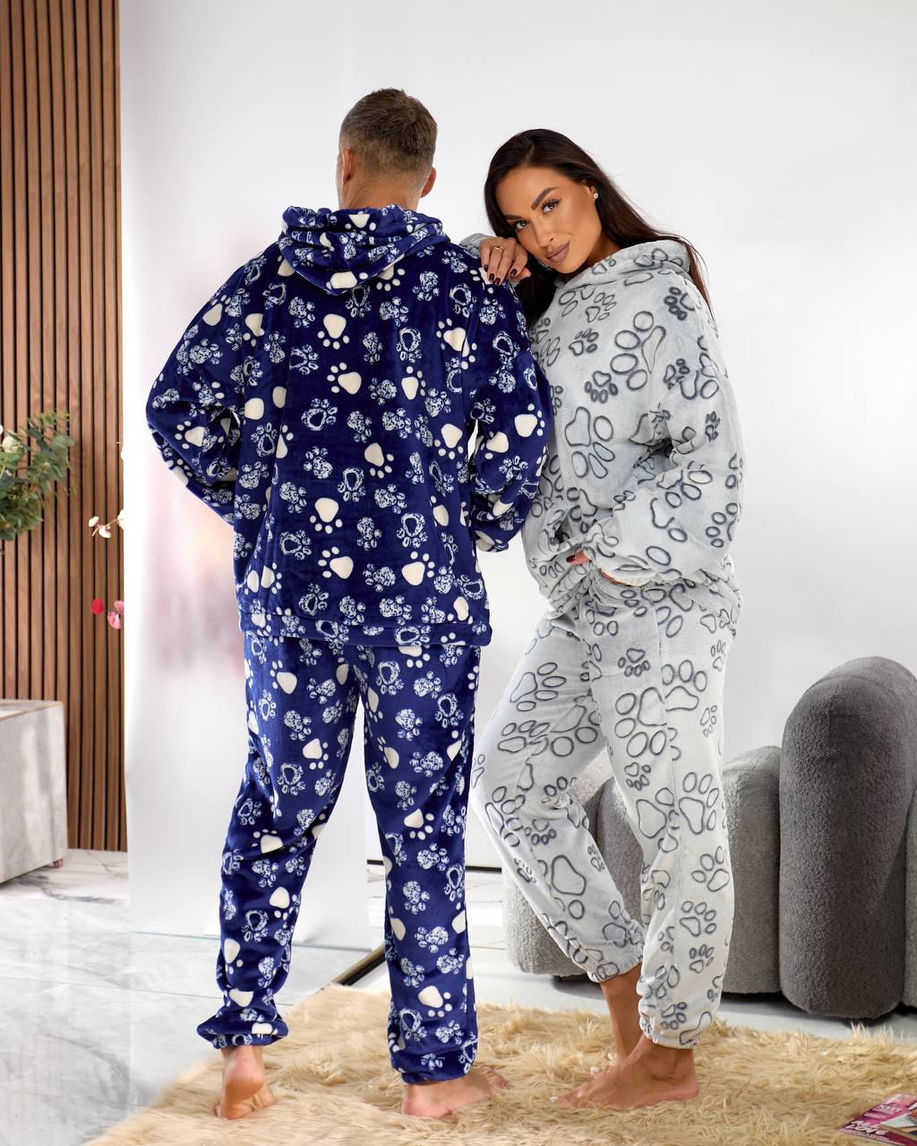 Two people wearing matching floral onesies in a cozy living room.