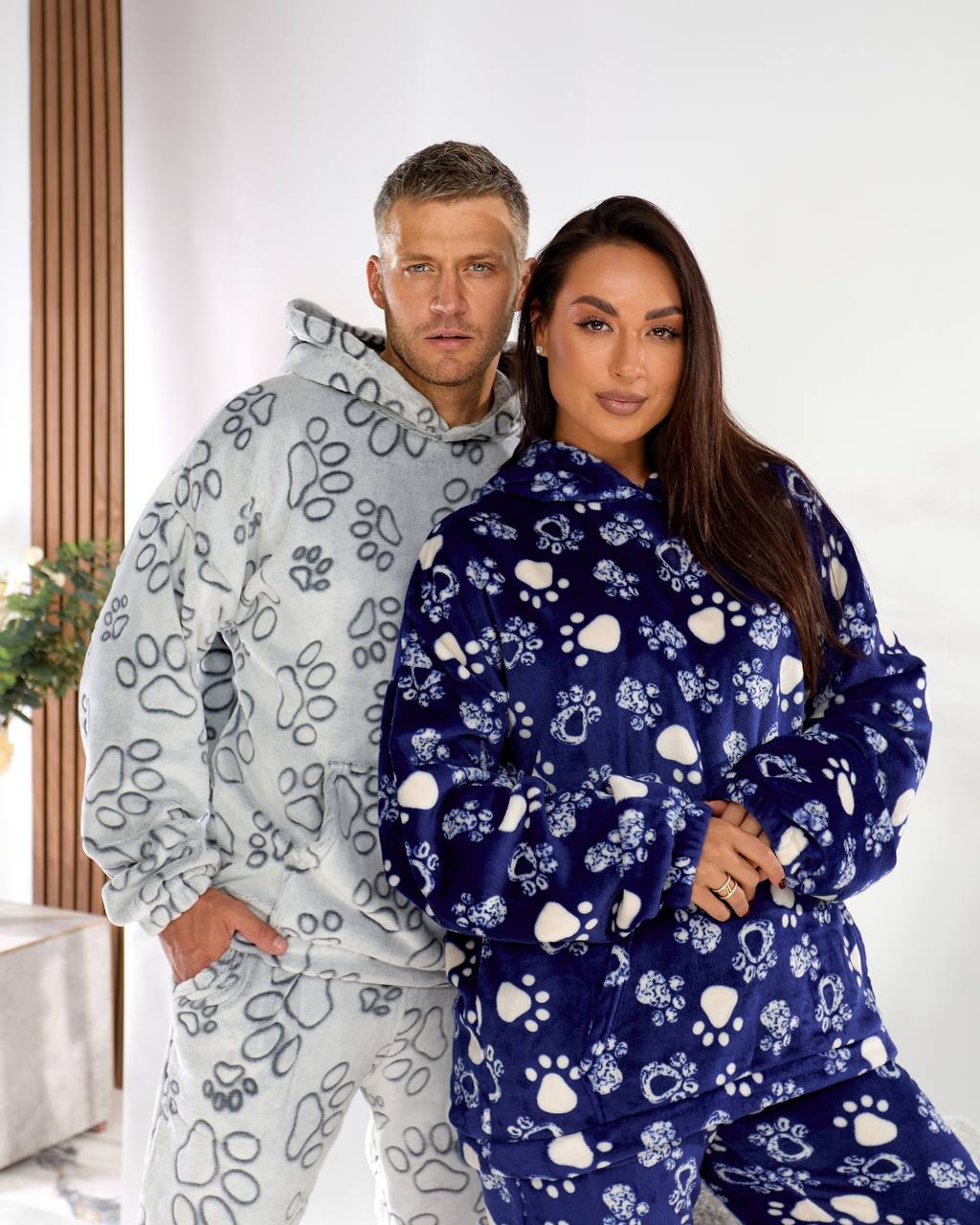 Two people wearing matching pajama sets with paw prints on a white background