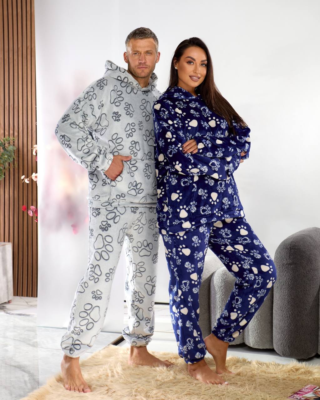 Two people wearing matching pajama sets with paw prints in a living room setting.