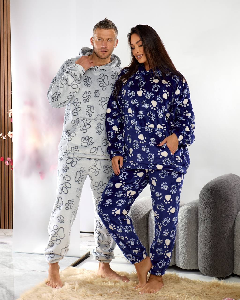 Man and woman wearing matching pajama sets with dog bone patterns in a living room.