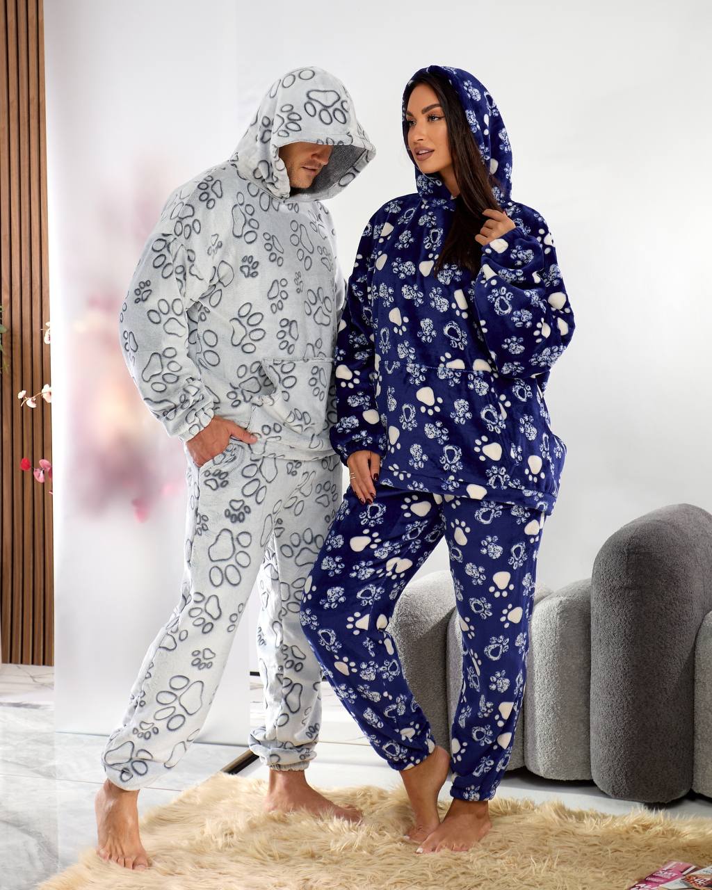 Two people wearing floral-patterned onesies in a living room setting.