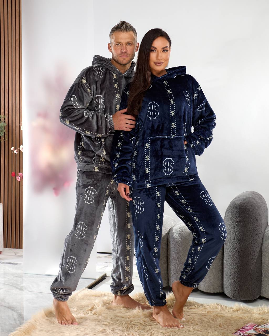 Two people wearing matching pajama sets with a brand logo in a living room.