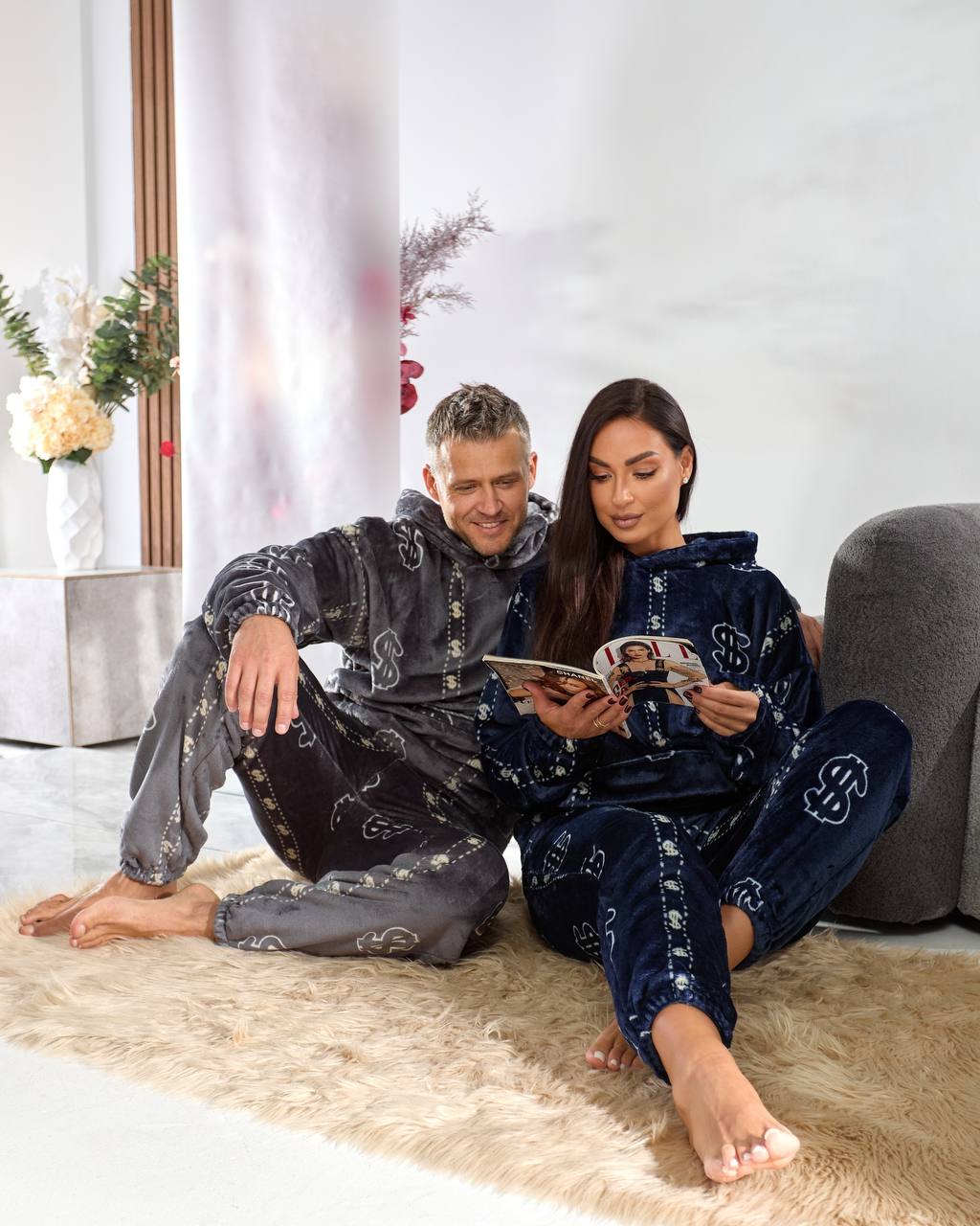 Man and woman sitting on a rug reading a magazine in a modern living room.