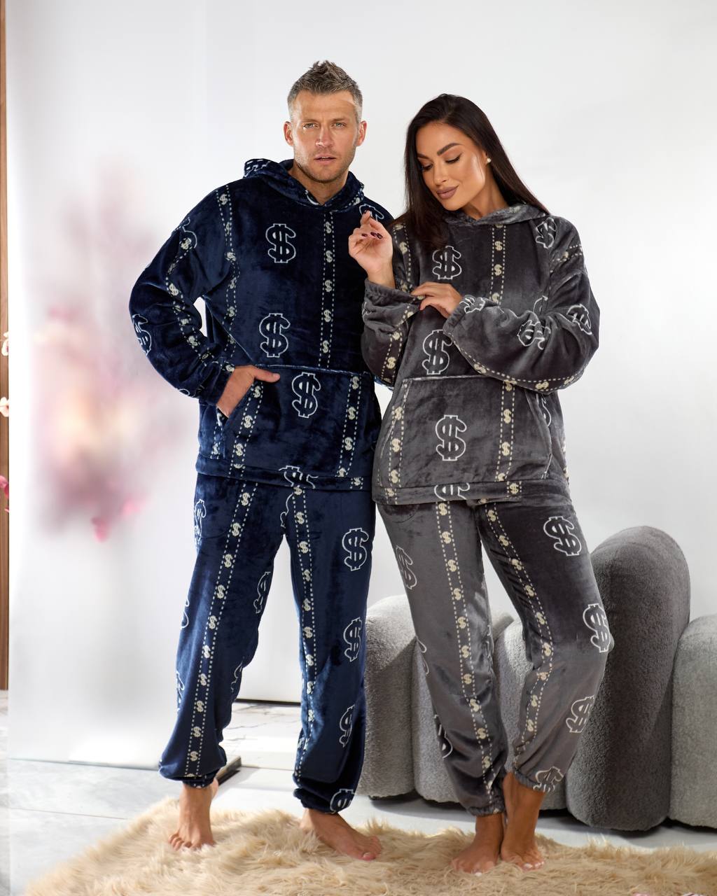 Two people wearing matching navy and gray pajama sets with dollar sign patterns in a room.