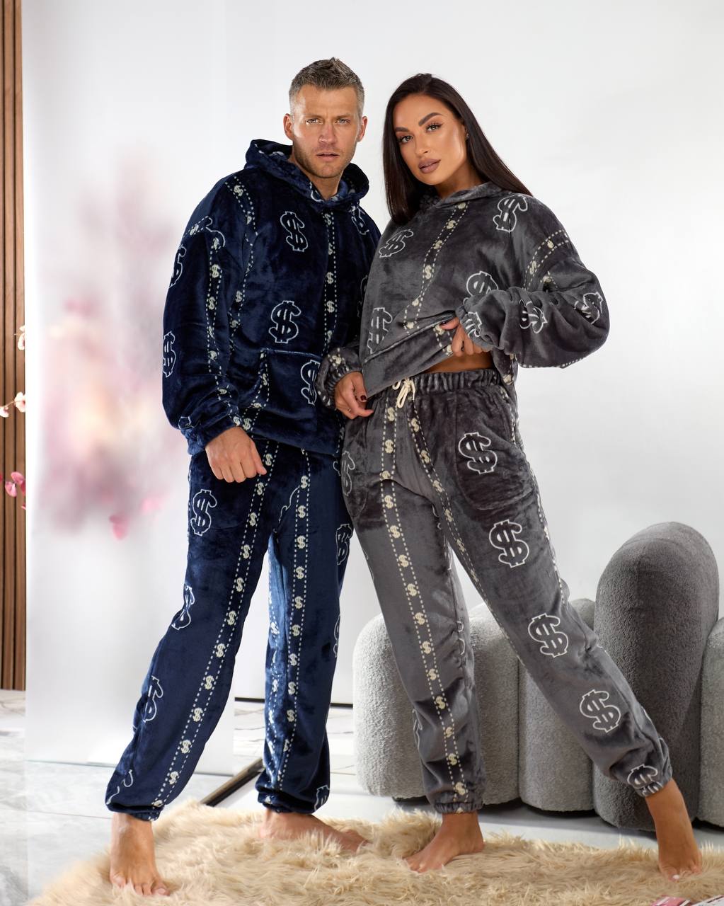 Two people wearing matching outfits with a brand logo in a living room setting.