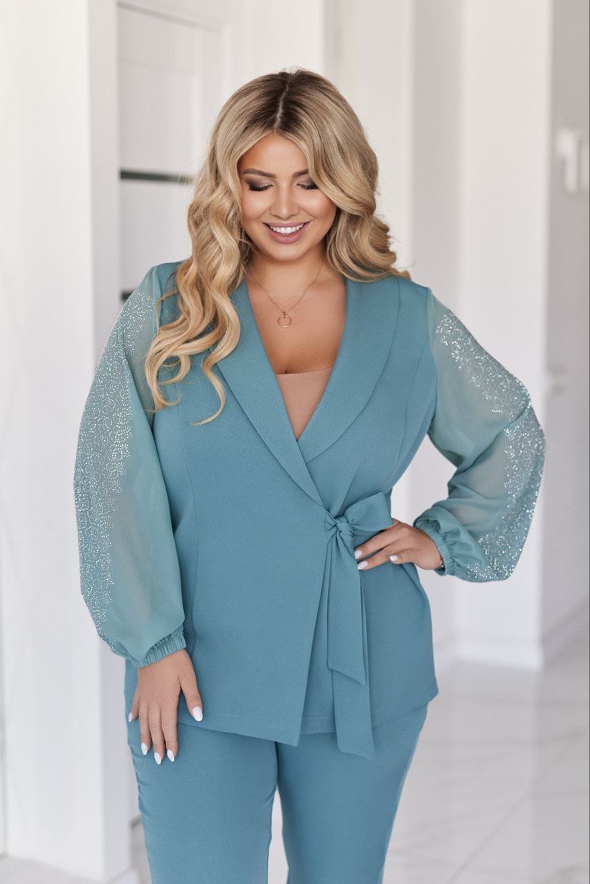 Woman wearing a teal outfit with sheer sleeves against a white background