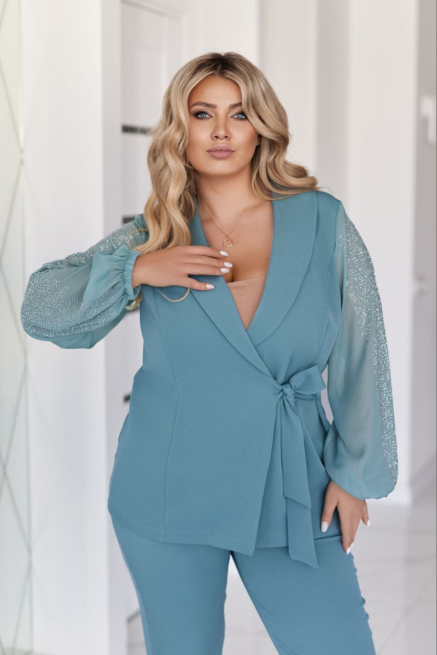 Woman wearing a teal outfit with embellished sleeves against a white background