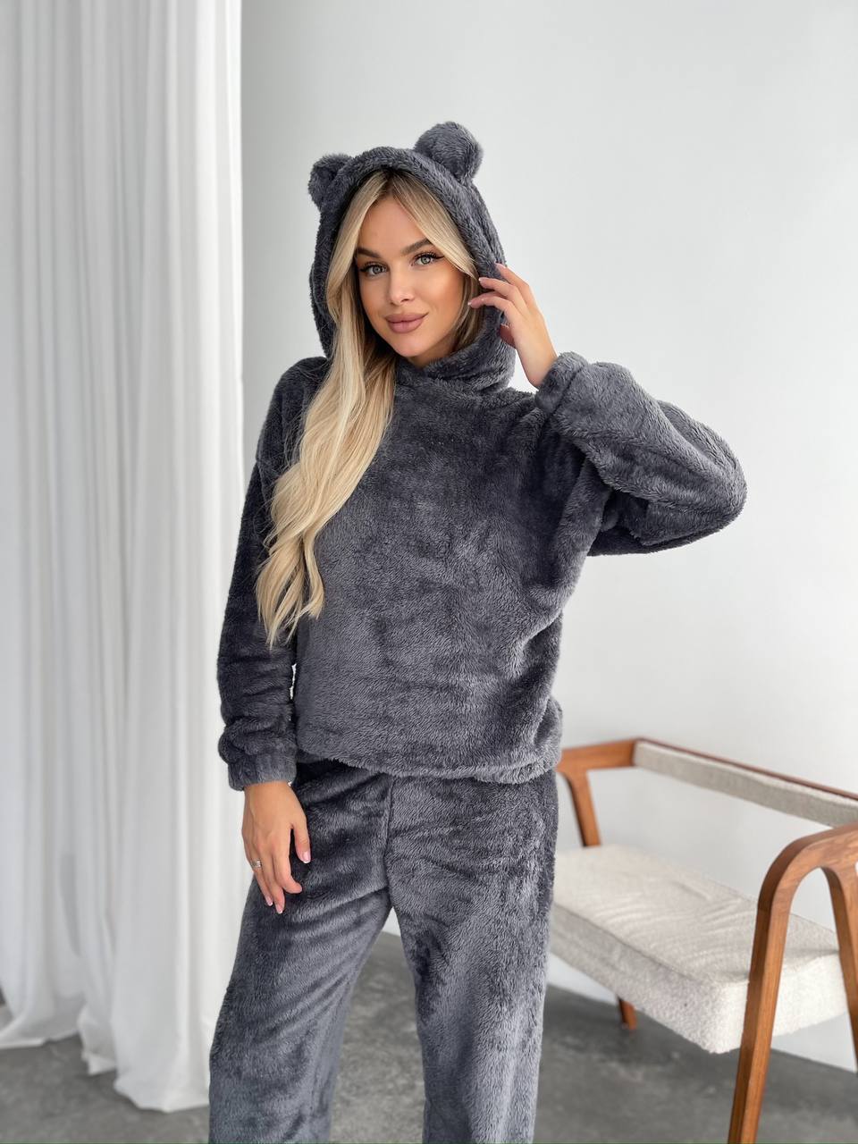 Woman wearing a gray hoodie with bear ears in a room with white walls and a couch.