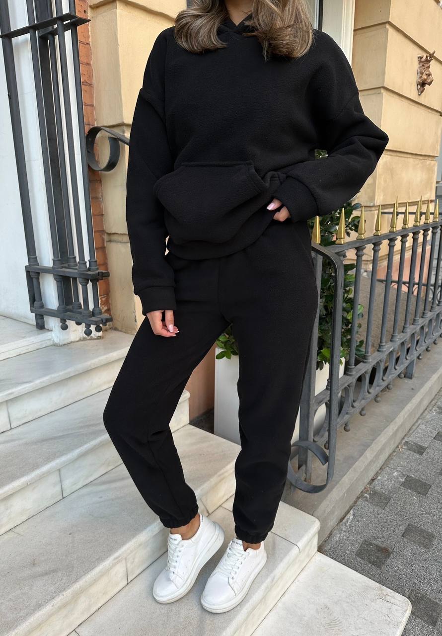 Person wearing a black outfit with white sneakers standing on steps.