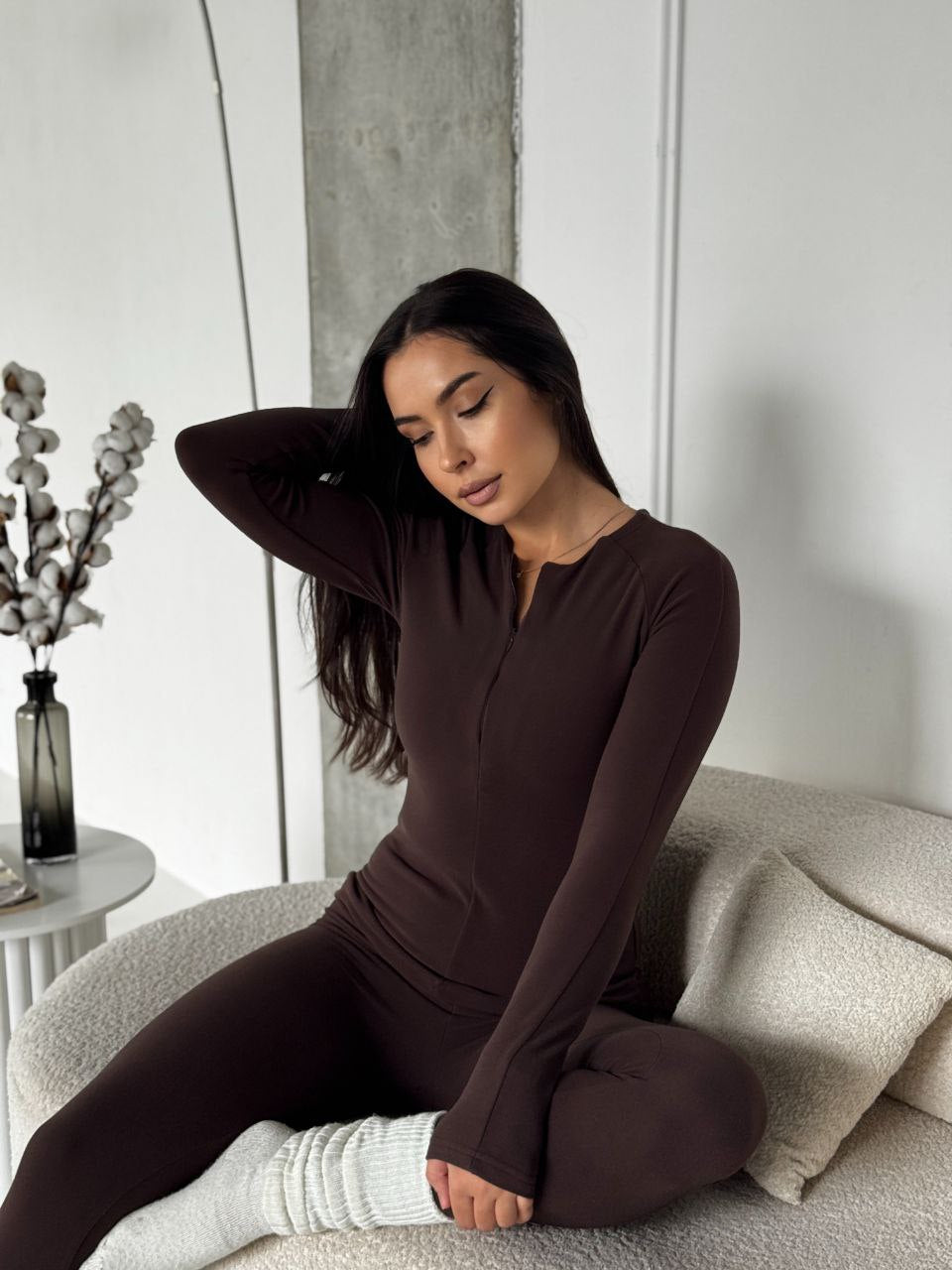 Woman in brown loungewear sitting on a couch in a minimalistic room.
