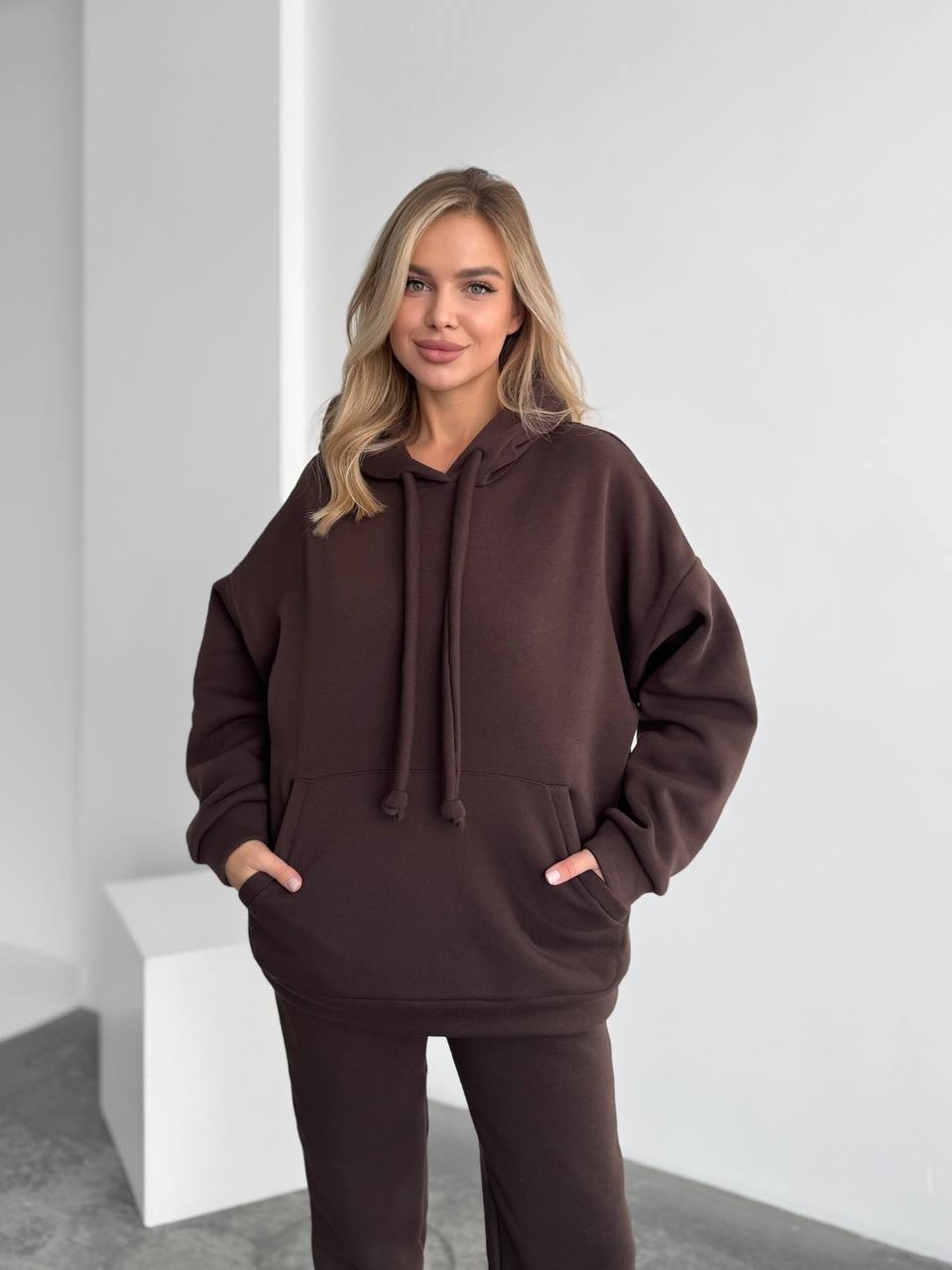 Woman wearing a brown hoodie and pants against a white background