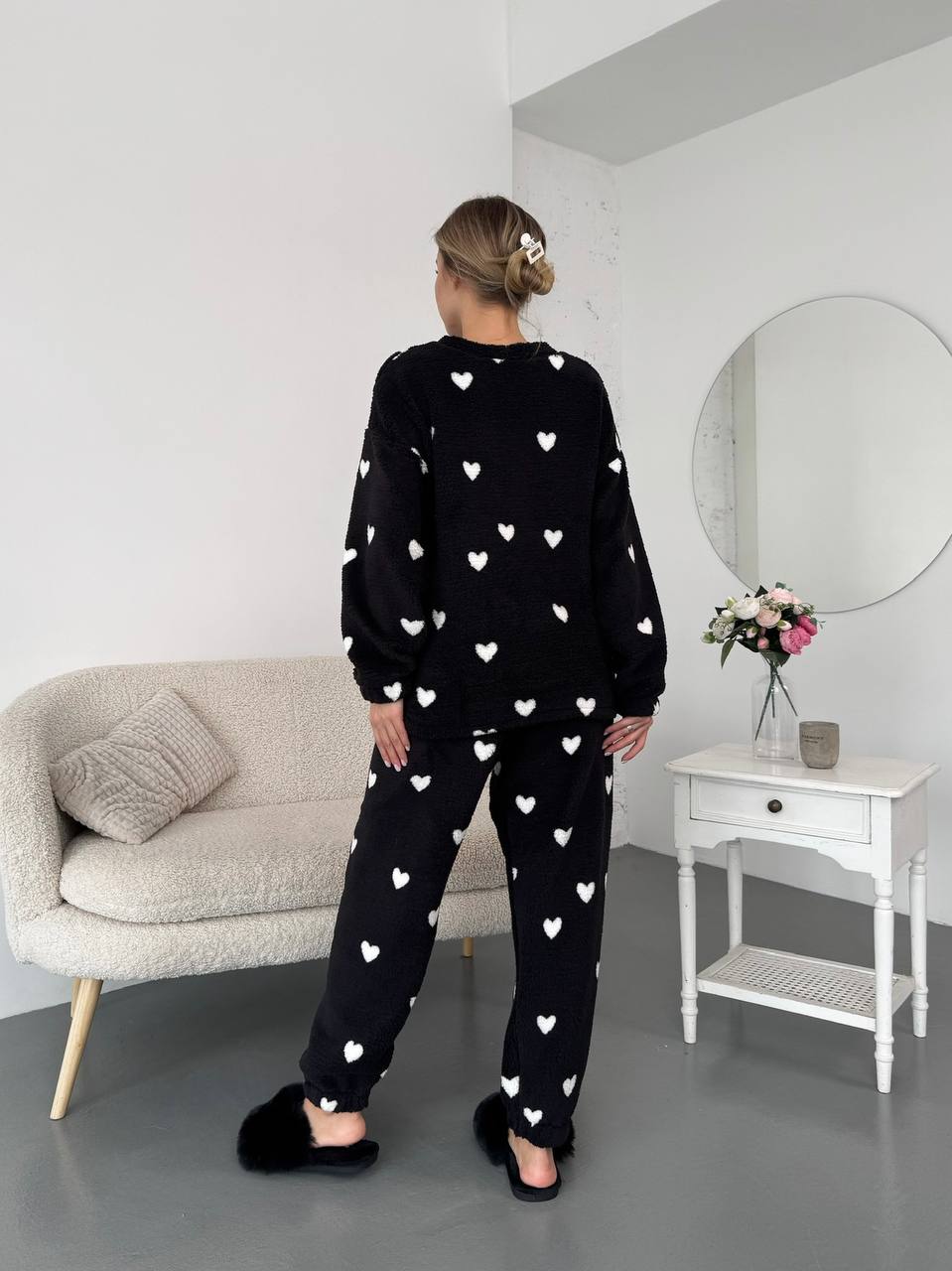 Person wearing a black pajama set with white heart patterns in a room.