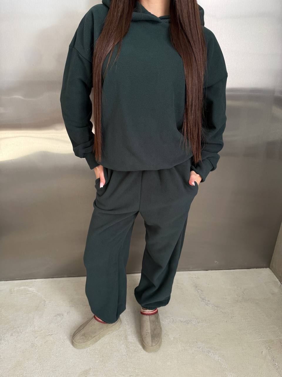 Person wearing a dark green hoodie and matching pants against a neutral background