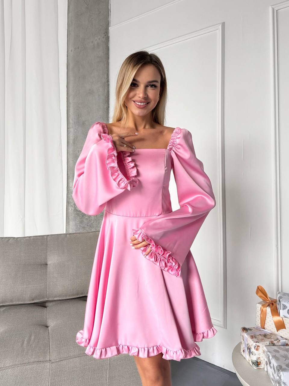 Woman wearing a pink dress with ruffled details in a room.