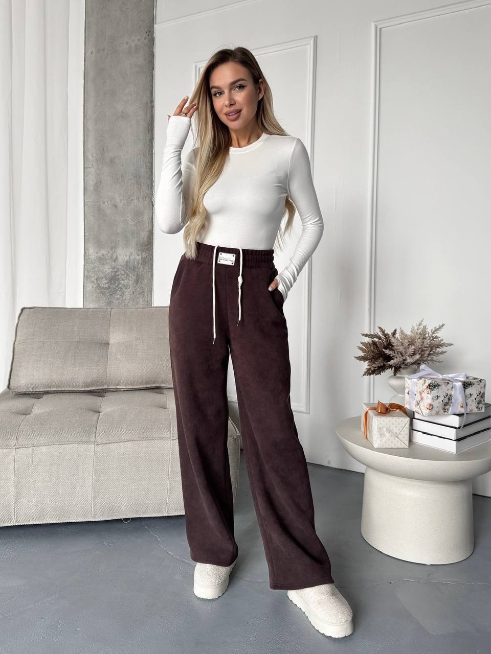 Woman in a white top and brown pants standing in a modern living room.