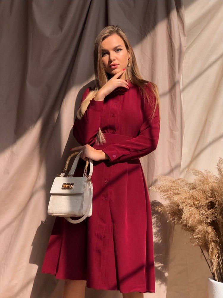 Woman in a red dress holding a white handbag against a neutral background