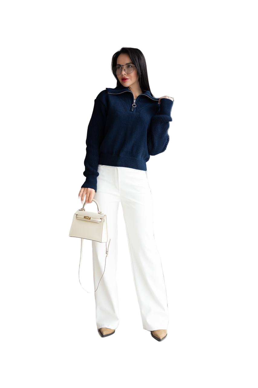 Woman wearing a navy blue sweater and white pants, holding a beige handbag on a white background