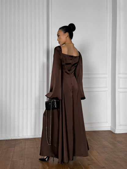Woman in a brown off-shoulder dress standing against a white paneled wall.