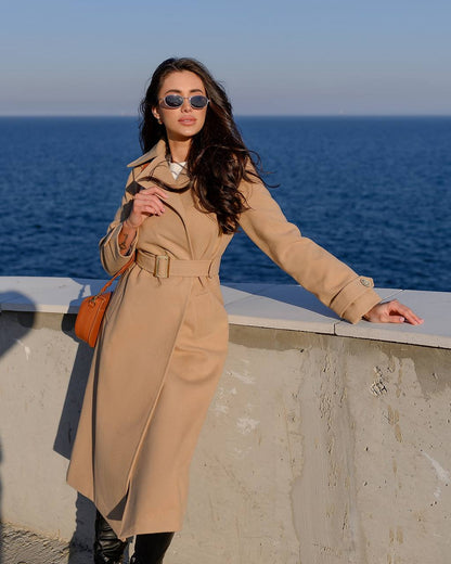 Woman in a beige trench coat standing by the ocean