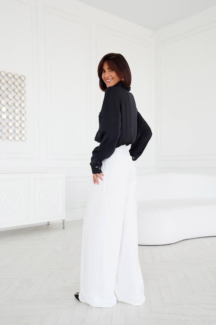 Woman wearing a black top and white pants in a minimal white room