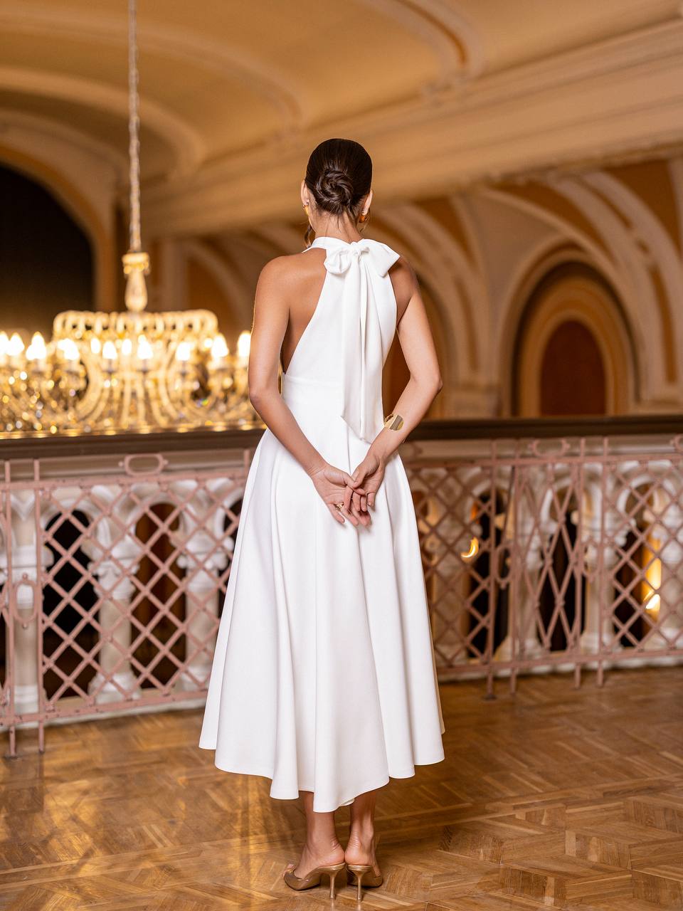 Woman in a white dress standing in an elegant interior setting with chandeliers.