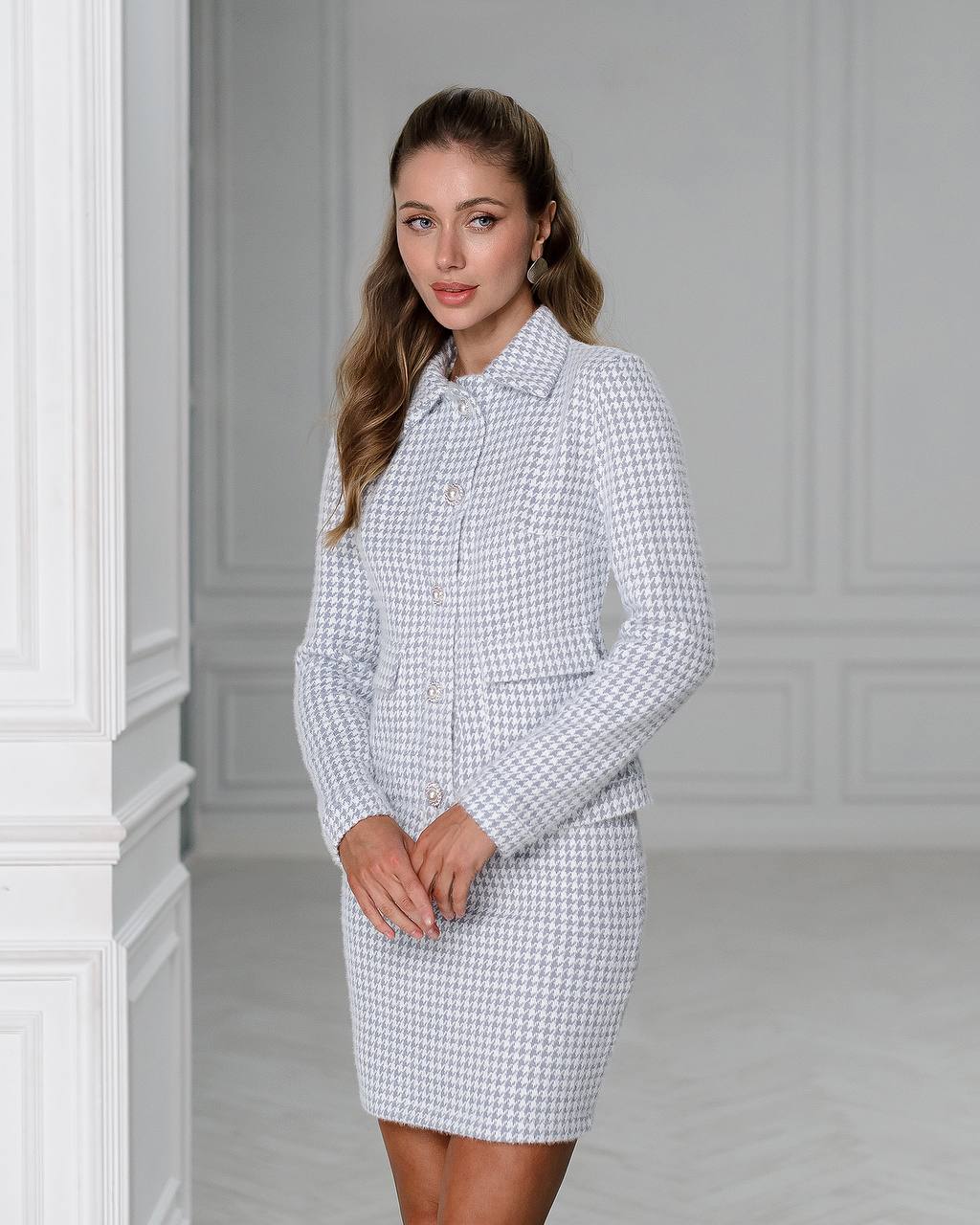 Woman wearing a checkered dress and jacket set against a gray wall.