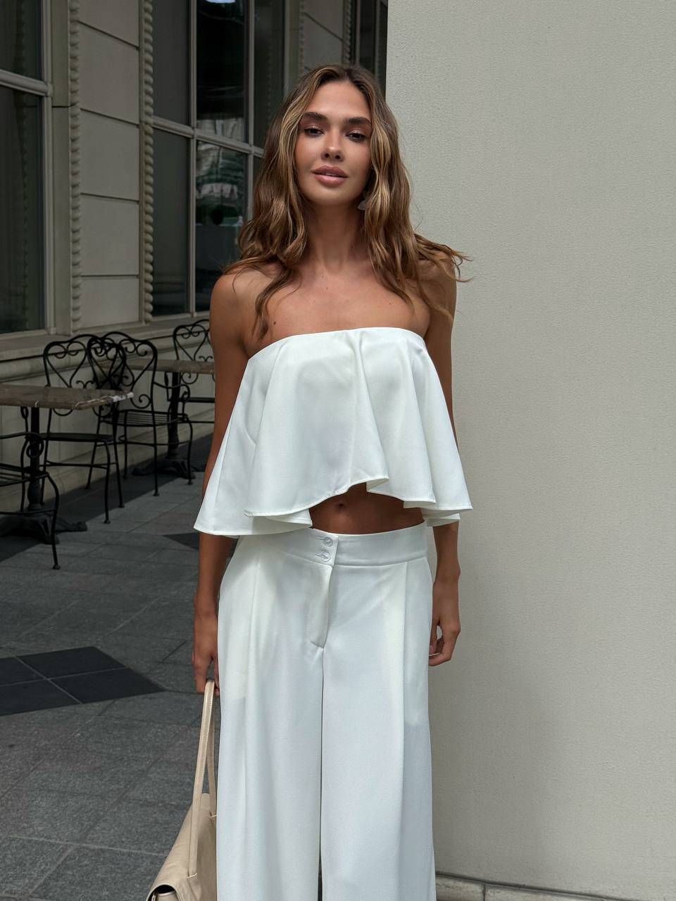 Woman wearing a white strapless top and light blue pants standing outdoors.