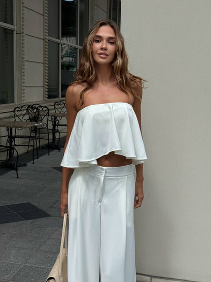 Woman wearing a white strapless top and light blue pants standing outdoors.