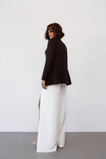 Person wearing a black blazer and white pants against a plain background