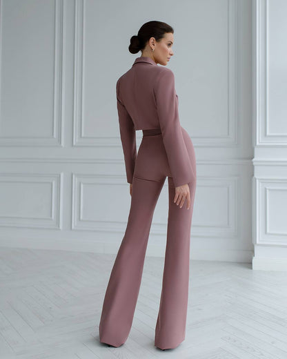 Woman wearing a mauve suit standing in a room with white walls and floor.