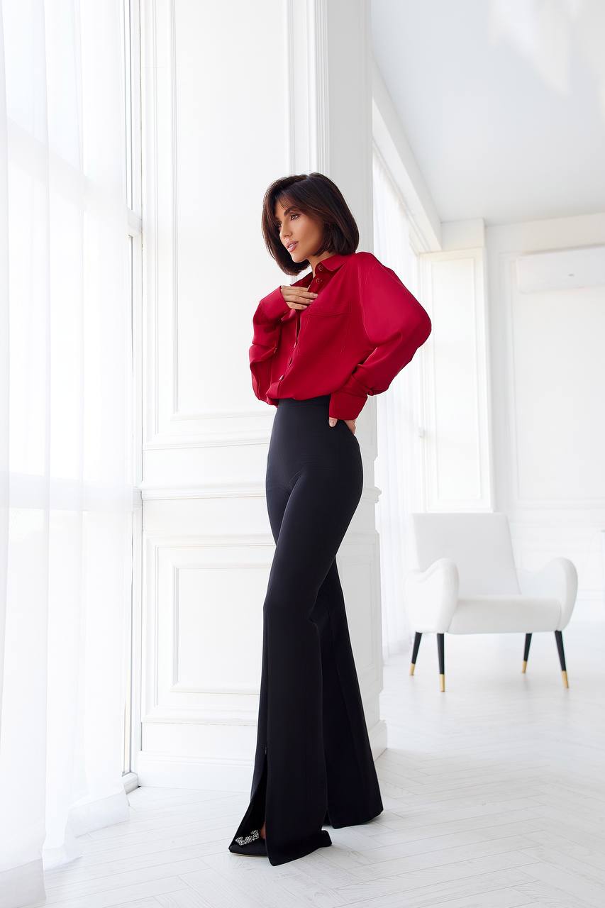 Person wearing a red blouse and black pants in a minimalistic room.
