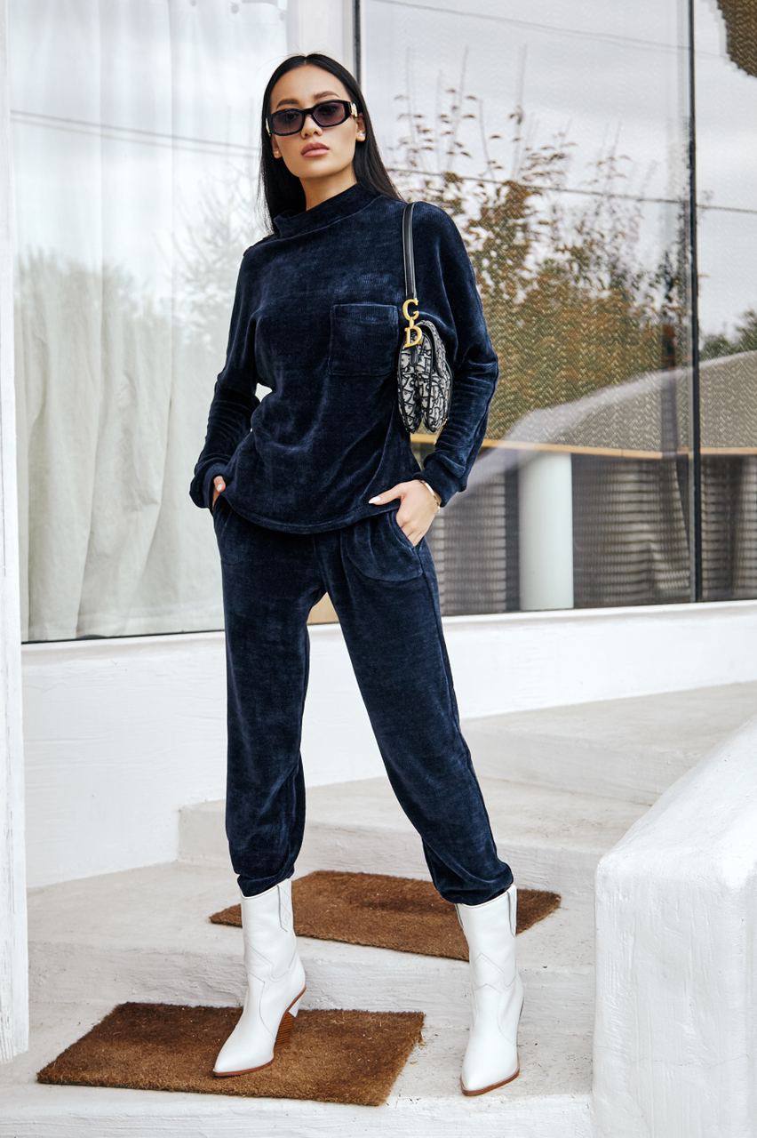 Woman in navy velvet outfit with white boots standing on a staircase.