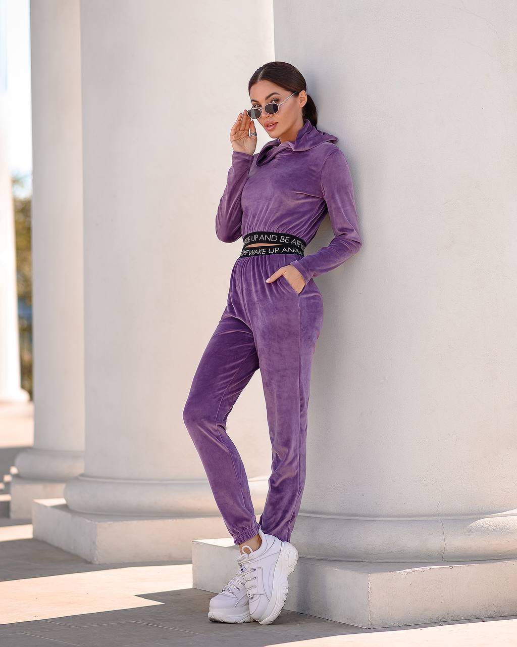 Woman in a purple tracksuit standing against a classical building.