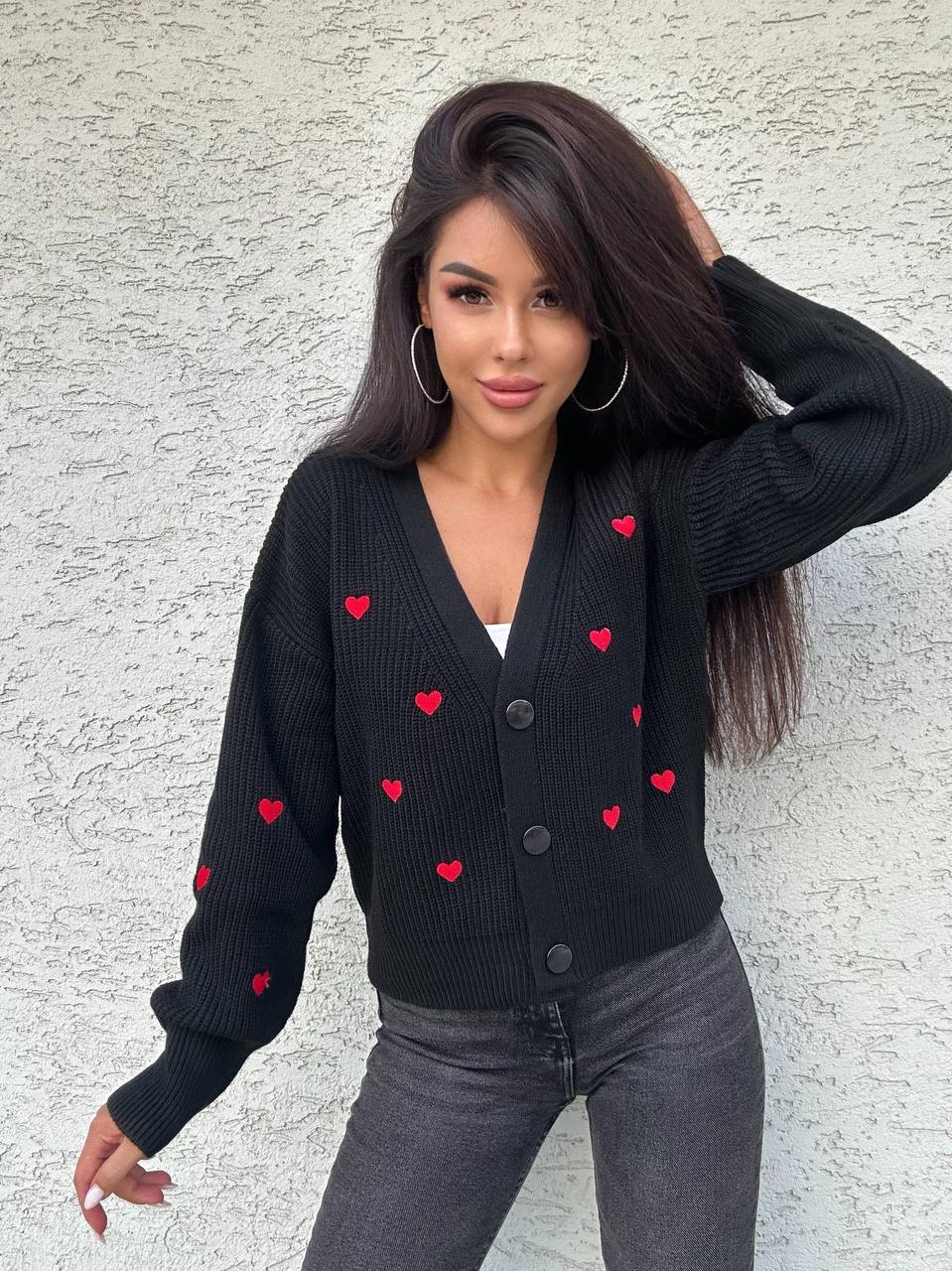 Woman wearing a black cardigan with red heart patterns against a light gray background