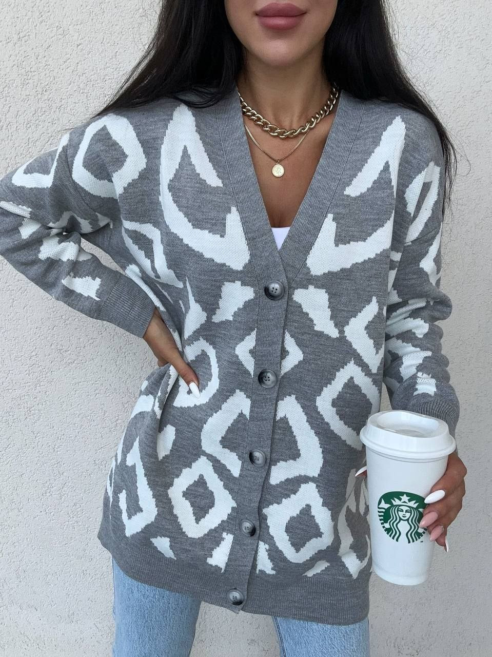 Person wearing a gray patterned cardigan holding a Starbucks cup against a neutral background