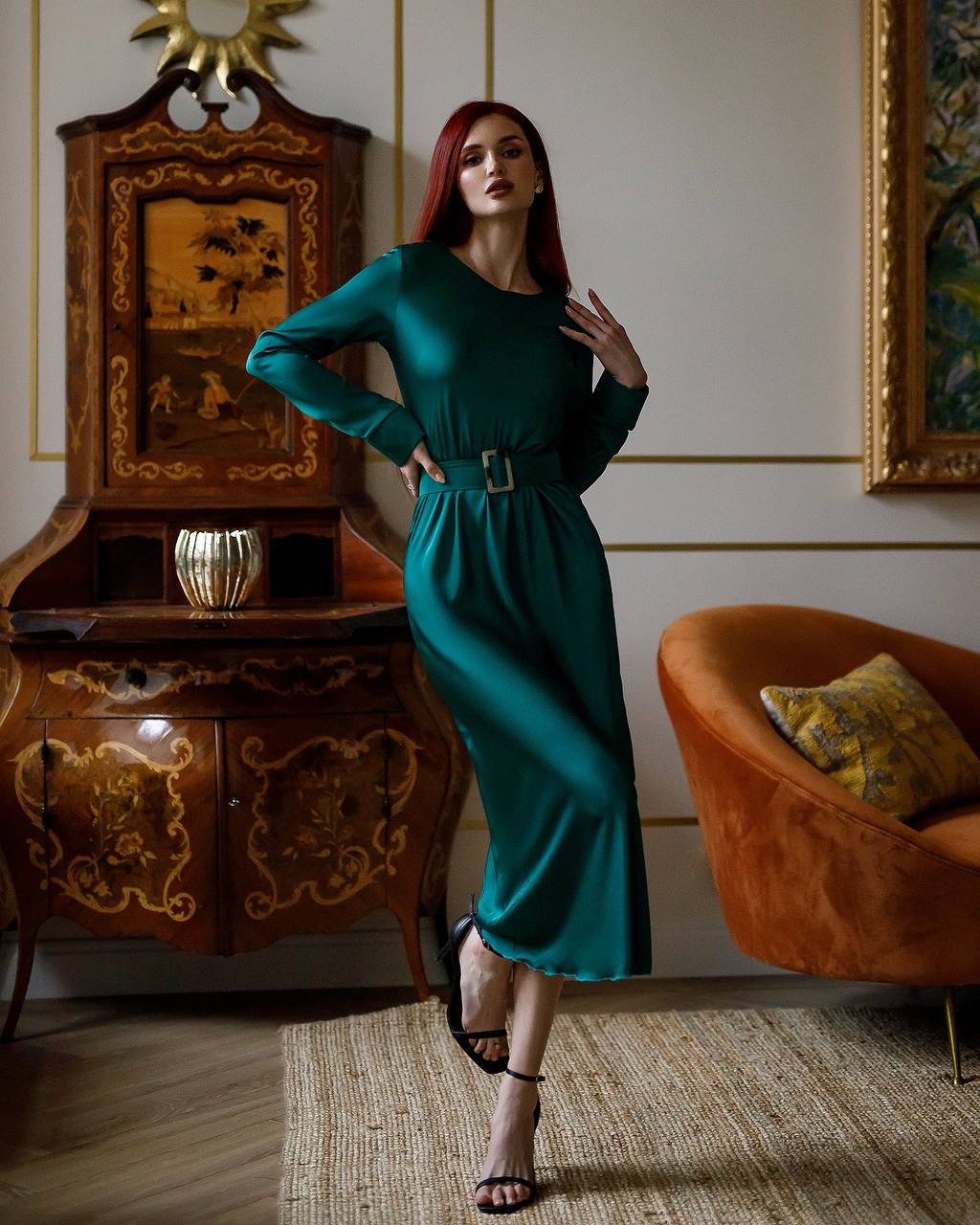Woman in a teal dress standing in an elegant room with ornate furniture.