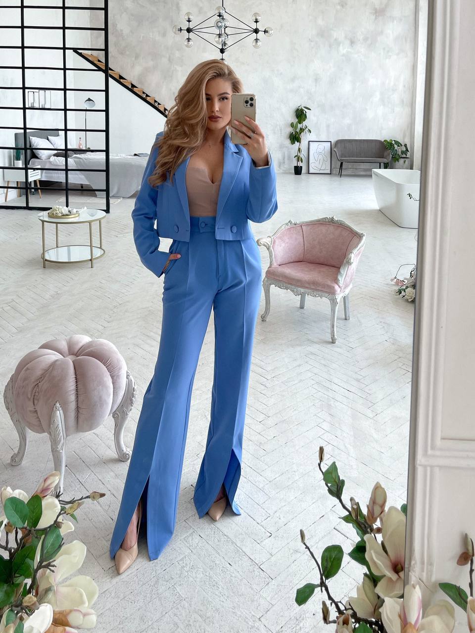 Woman in a blue suit taking a mirror selfie in a stylish room.
