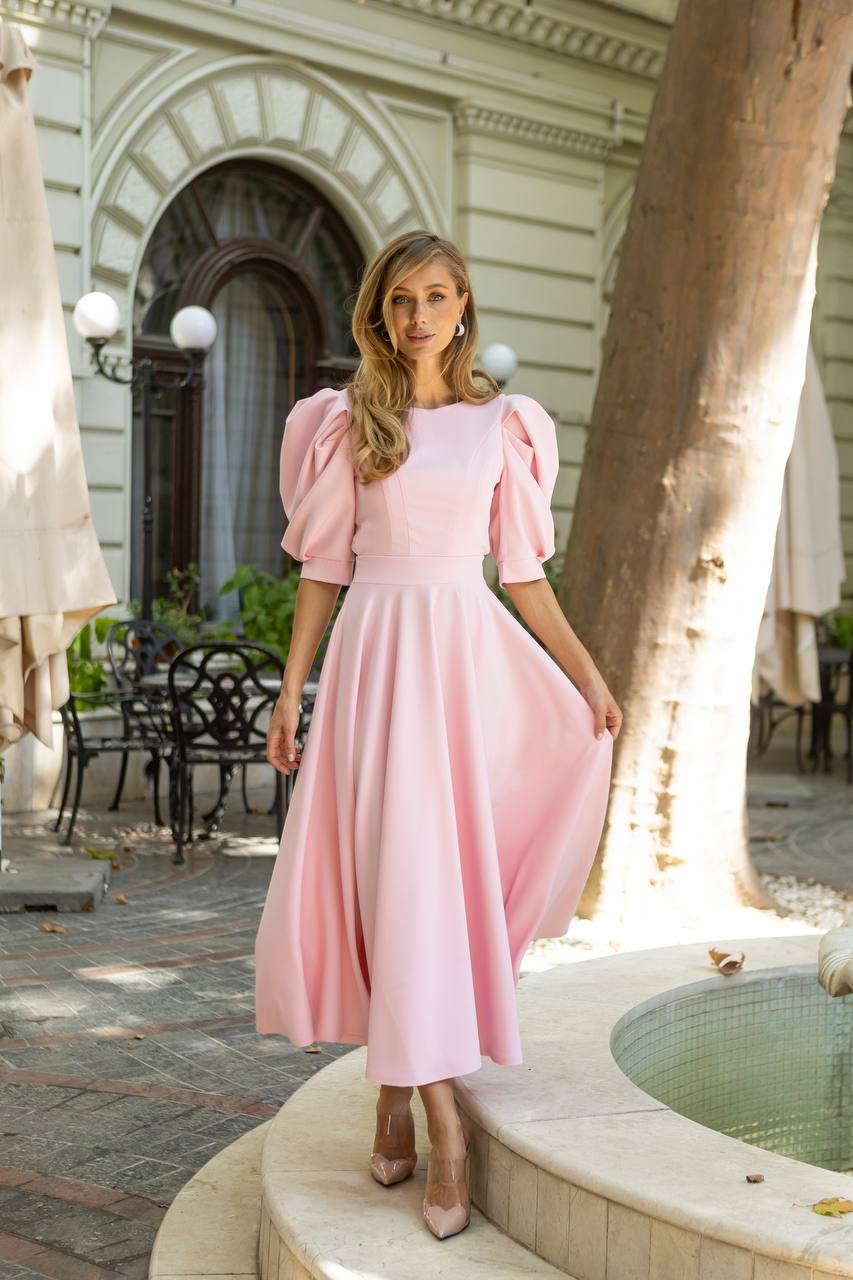 Woman in a pink dress standing outdoors near a building entrance.