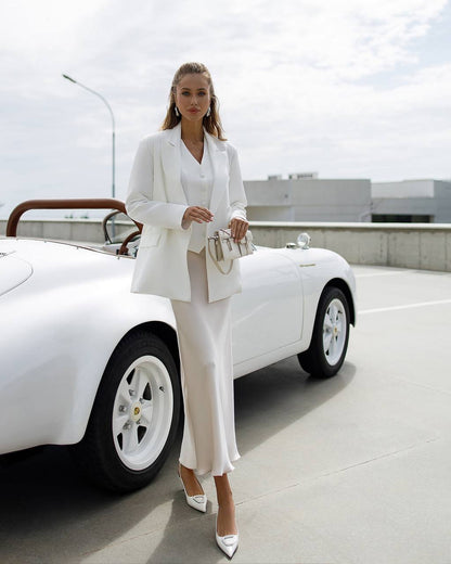 Woman in a white suit standing next to a white car on a rooftop.