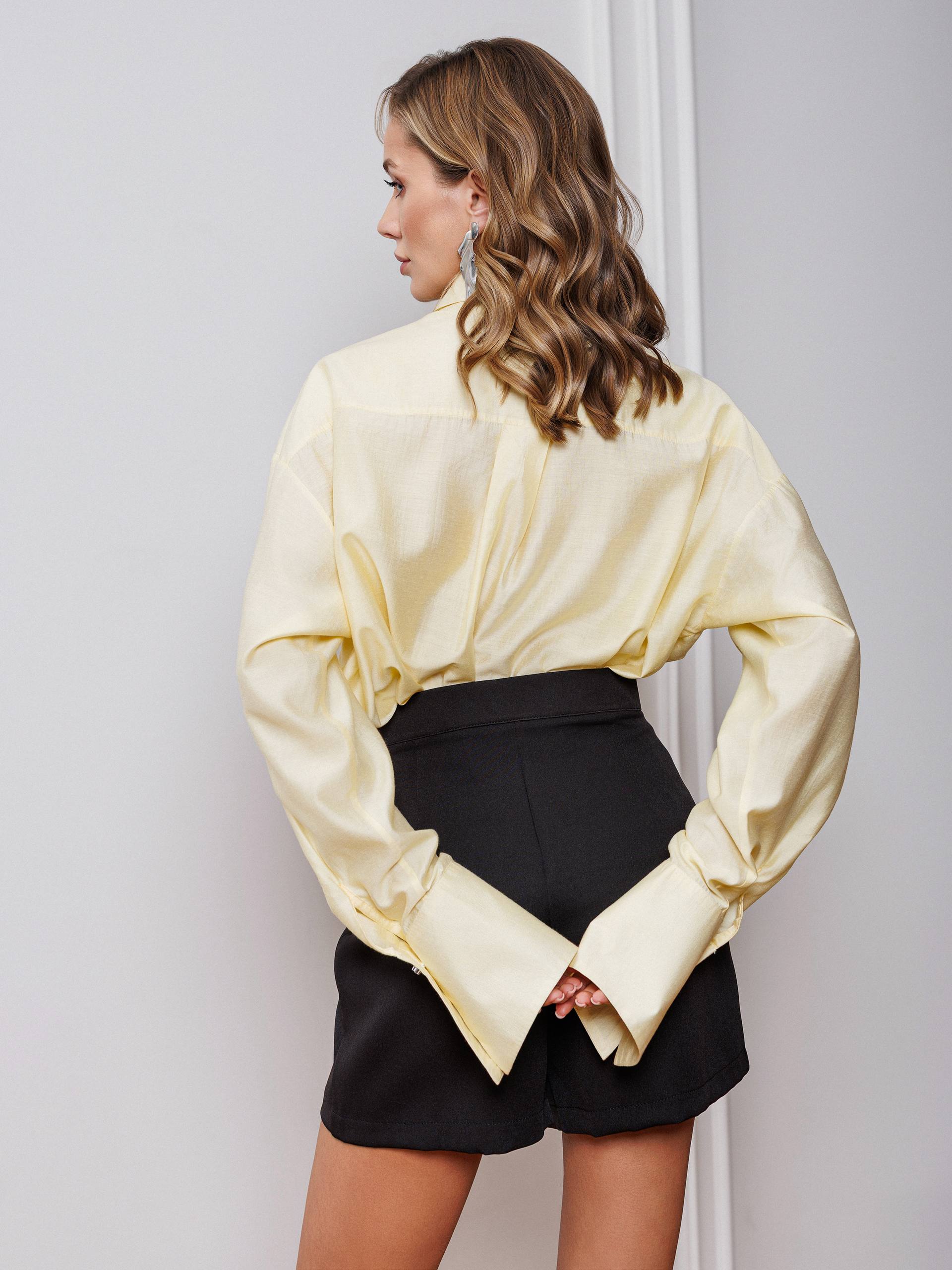 Woman wearing a light yellow blouse and black shorts against a plain background