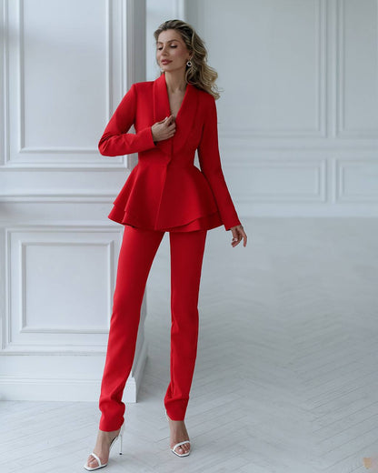 Woman wearing a red suit standing against a white wall.