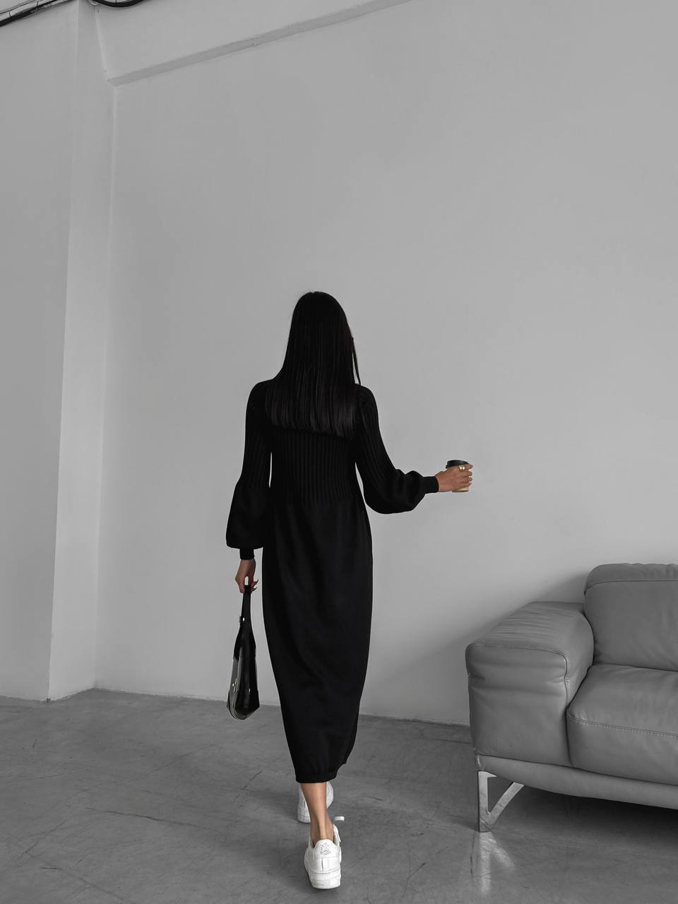 Person wearing a black dress walking in a minimalistic room with a gray sofa.