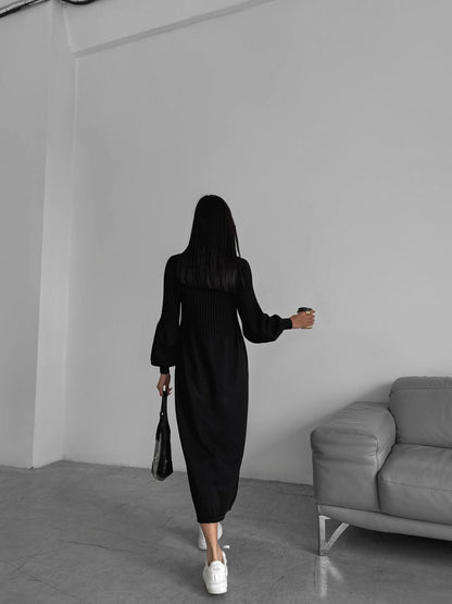 Person wearing a black dress walking in a minimalistic room with a gray sofa.
