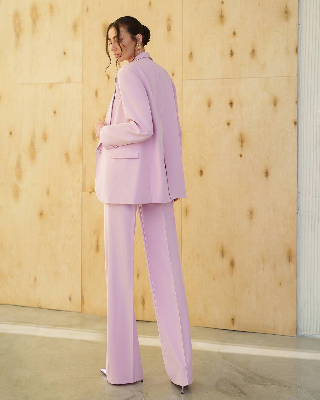 Woman wearing a light purple suit standing against a wooden wall.